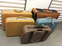 Five luggage pieces including three hard shell cases (one blue Samsonite, two yellow Boyle) and two fabric suitcases (gray with brown leather accents, orange and black).