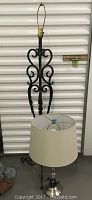 Full view of wrought iron floor lamp without shade or finial, showing swirl and leaf details, along with new table lamp with shade in front