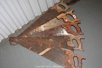 Five vintage hand saws laid out, showing wooden handles and rusted blades.