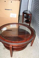 Large round wood coffee table with glass top, three tiers, and protective edge cover. Dark wood with some scratches.