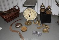 Overall view of collection on floor showing Hanson utility scale, scythe, brass pieces, basket with keys, cobbler's tools.