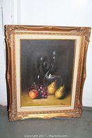 Full view of the framed still life oil painting showing fruits and a glass decanter on canvas.