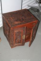 Full view of hand carved camphor chest with open front doors showing detailed carvings on top and doors and glimpse of internal storage.