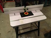 Overhead view of white laminate tabletop showing router insert ring and fence