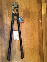 Full view of the 30 inch bolt cutter with black handles and grips on a wooden surface, alongside a small paper marked '5'.