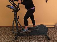 Side view of grey elliptical cross trainer showing frame profile, foot pedals and handlebars