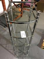 Front angle view showing five shelves made of glass held within a chrome frame with rounded posts.