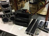 Wide view of the Panasonic stereo set with two speakers and remote, along with stacked Sony components and associated cables on a table.