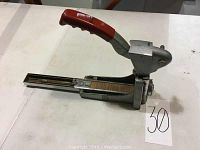 Full side view of the Rosetto carton stapler showing the red handle and metal base with staples loaded in the magazine.