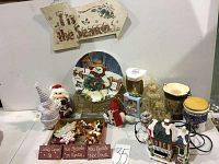Photo showing assortment of holiday decorations including figurines, mini houses, signs, and containers arranged on a white surface.