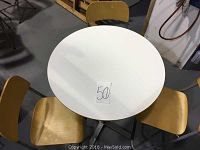 Top view of the white round pedestal table with three beech wood folding chairs around it.