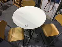 Full set showing white round IKEA pedestal table surrounded by three folding chairs with beech wood seats and metal frames in warehouse setting.