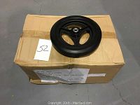 Photo of a single black 11-inch diameter wheel with three spokes and housed bearings on top of a box