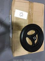 Top view of one of the wheels on a brown box, showing black solid rim and three-spoke design with central bearing.