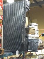 Black plastic 6 foot truck bed liner positioned vertically on shelving, ribbed surface visible, part of storage area with boxes around.