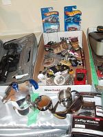 Photo showing Bialetti stovetop espresso maker, chrome cream and sugar set, Hot Wheels cars in packaging, iCarPlay Wireless device, and assorted toy cars and pins arranged in boxes.