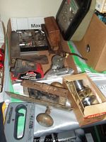 Photo showing vintage and modern door handles boxed, Jobmate laser level with red casing, some old wooden hand planes, and various small tools.