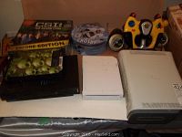 Photo showing the CSI board game box, stacked CD/DVD cases, white Xbox 360 console, white Wii RVL-001 console, and yellow Power Wheel 30 game system controller.