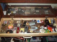 Wide view of the case interior showing the assorted vintage pinback buttons, knives, watches, flashlight, and other small items spread inside the open wooden display case.