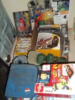 Photo showing boxed Ed Hardy seat cover, pop rock karaoke CD pack, some CDs, green padded item, and blue Pepsi case with other toys and electronics around.