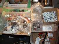 Overview photo of glass chandelier crystals inside a plastic container, box of Delft blue style ceramic thimbles, batteries, and other small items on a table.