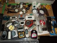 Several watches, MP3 players, digital timers, mini vacuum, precision mini driver, knives and Canada patches spread on table.