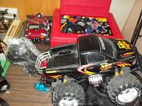 Black remote-controlled Dodge XT 4x4 truck with large off-road tires, flame decals, and 18L motor shown on tabletop with other items behind