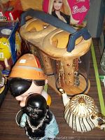 Jewelry display case with necklaces, Pinocchio head bank, Barbie suitcase, sewing box, Sadler teapot, and laughing Buddha figure arranged on surface.