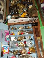 Photo showing trays filled with assorted earrings, brooches, pins, and small jewelry pieces in various materials including gold-tone and silver-tone finishes.