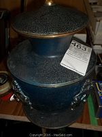 Photo showing side view of the blue patina brass urn with lid and ornate handles and auction lot tag attached.