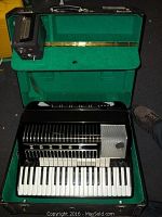Accordion inside open hard case showing green felt interior and separate amplifier module
