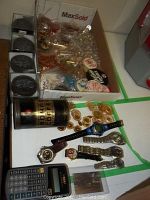 Photo of commemorative hockey pucks, wristwatches, a calculator, Bokar coffee container, and a box containing pinback buttons and chandelier crystals.