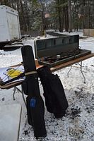 Polar LTD bow and arrows in original metal case with storage wear, two black golf bags standing upright beside the table.