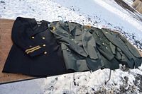 Four vintage military uniforms laid out on a table outdoors in snow, one Navy and three Army uniforms.