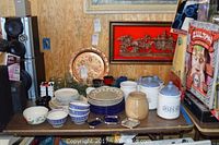 Wide view of the collection of handmade ceramic dinner plates, bowls, lidded kitchen containers, glassware, metal tray, and mugs arranged on a table.
