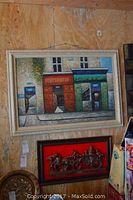 Framed oil painting on canvas of a Paris street scene with two storefronts and a mailbox, signed L.R. Davis. Below it is a framed painted plaster relief of a horse-drawn fire engine on a bright red background with some paint wear.