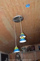 Photo showing three conical painted glass shades hanging from a round metal ceiling mount in a wooden room.