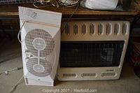 Photo of beige Glo Warm heater and white twin window fan side by side on a concrete floor.