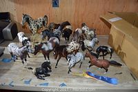 Overview of all sixteen horse figurines arranged on a table, showing various shapes, sizes, and color patterns including spotted and solid colors.