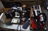 Overview of all cameras and items arranged on a table with some carrying cases and a red Guitar Hero controller in box