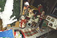 Photo showing the collection of Christmas decorations including a white fiber optic tree, ceramic snowman figurines, plush Santa Claus, and other small ornaments on a table.