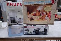 Photo showing the boxed Krups Heliora coffee maker, RTH hot pot, Volcano Punch Bowl, and Oggi 10-piece bar set arranged together.