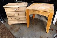 Two tables side by side on a concrete surface, showing a wood end table with drawers and a square laminate top table.