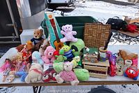 Overview of stuffed animals, dolls, guitar, and other items on a table outdoors
