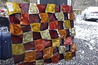 Full front view showing the colorful enameled metal squares arranged in a geometric pattern with red, orange, yellow, and cream shades on a metal backing.