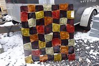 Full view of the geometric metal wall art set outdoors on gravel and snow showing an arrangement of colorfully enameled square and rectangular panels with a reflective glazed finish.