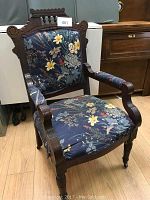 Front view of Victorian Eastlake wooden armchair with floral upholstery showing detailed carved wood frame and armrests. Cushion upholstery is loose.