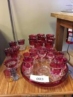 Photo showing the full collection of various sized ruby flashed glasses and a large serving plate on a wooden table.