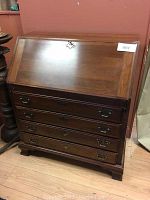 Front view of closed drop front desk showing four drawers, brass hardware, bracket feet.