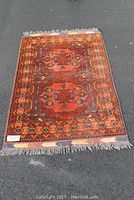 Full view of hand knotted runner rug laid out on pavement showing overall geometric pattern in shades of red, brown, and blue with fringed ends